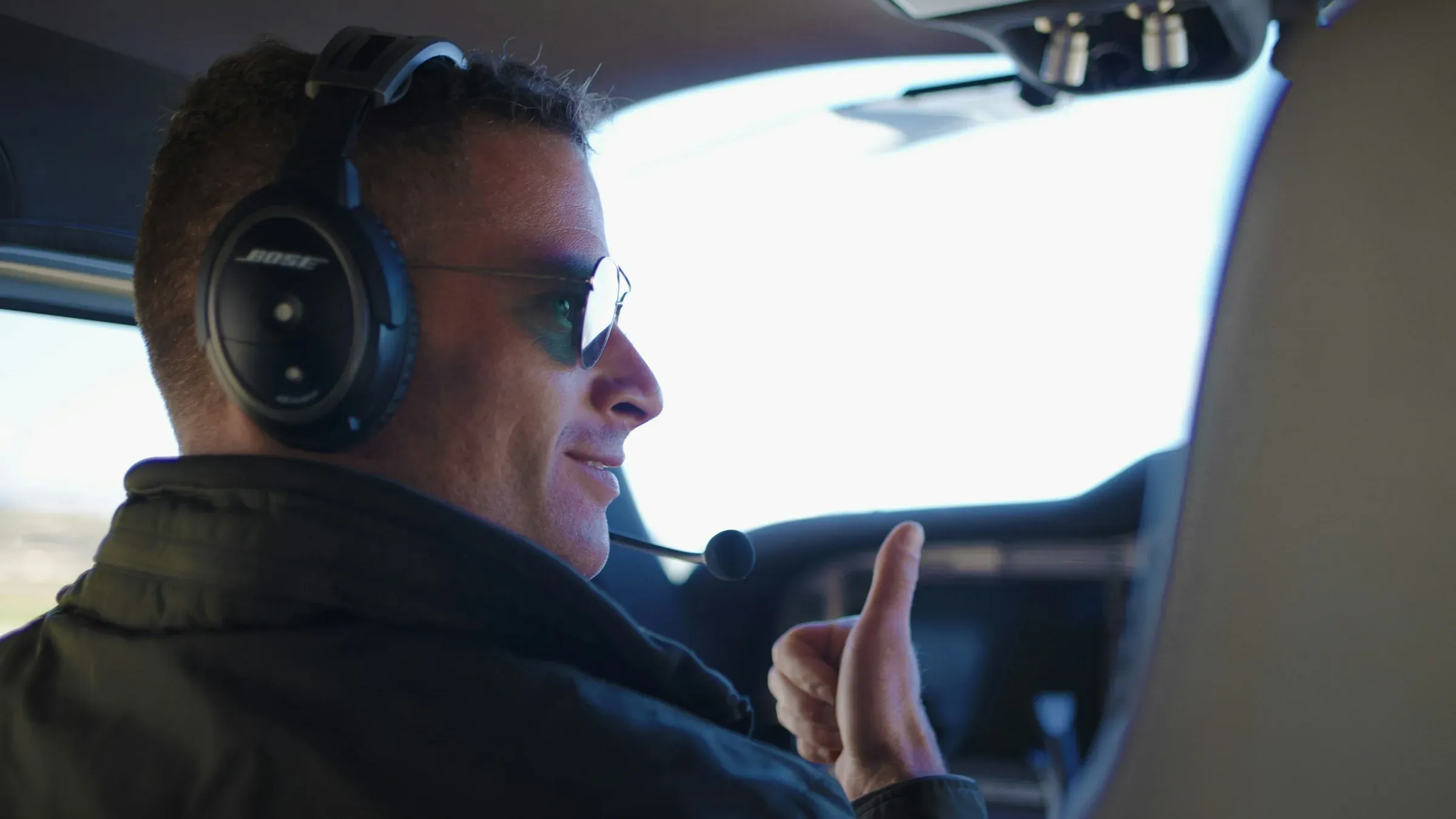 A pilot in a headset giving a thumbs-up from the cockpit of a small plane